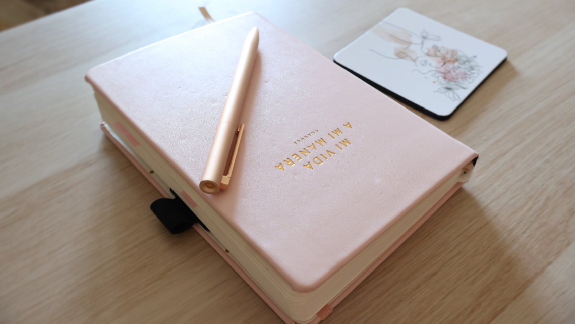 Cuaderno rosa con bolígrafo dorado y posavasos