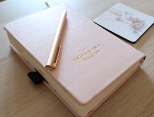 Cuaderno rosa con bolígrafo dorado y posavasos